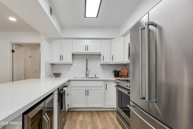 kitchen with beverage cooler, a sink, white cabinets, appliances with stainless steel finishes, and tasteful backsplash