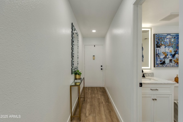 hallway with a sink, visible vents, baseboards, and wood finished floors