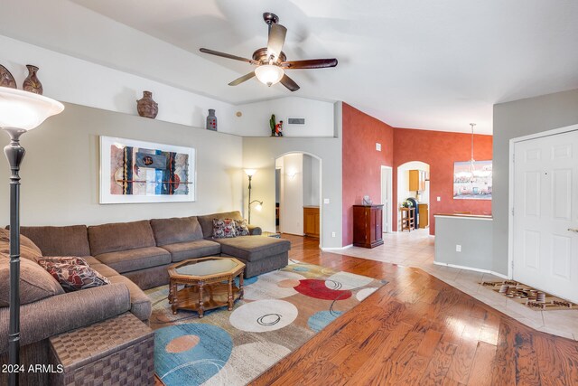 living room with ceiling fan with notable chandelier, vaulted ceiling, and tile flooring