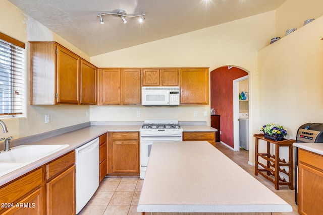 kitchen with white appliances, rail lighting, light tile floors, vaulted ceiling, and washer / dryer