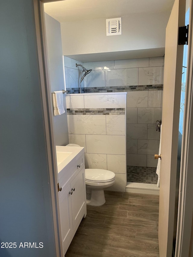 bathroom featuring hardwood / wood-style flooring, vanity, toilet, and a tile shower