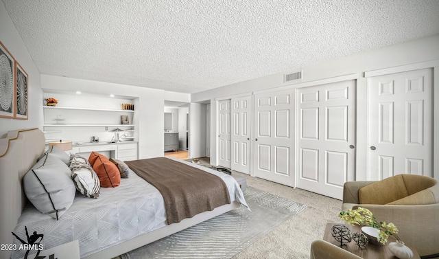 bedroom with a textured ceiling, light carpet, visible vents, multiple closets, and built in desk