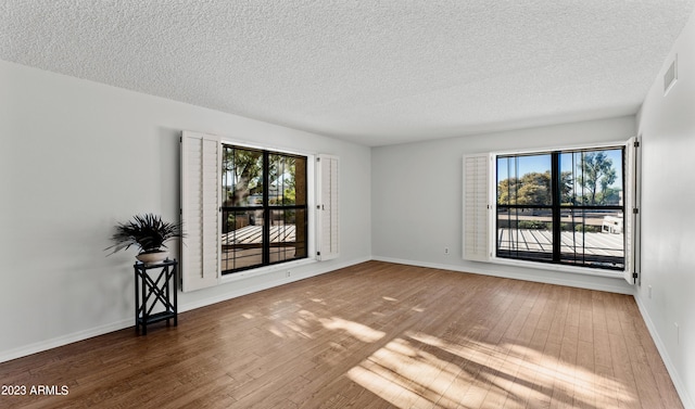 unfurnished room featuring a healthy amount of sunlight, baseboards, visible vents, and hardwood / wood-style floors