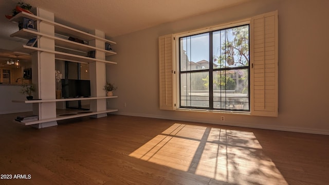 unfurnished living room featuring a textured ceiling, wood finished floors, and baseboards