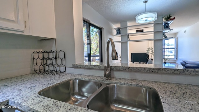 kitchen with light stone counters, visible vents, white cabinets, a sink, and a textured ceiling