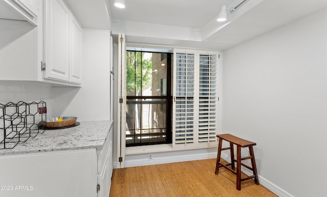 kitchen featuring light wood-type flooring, white cabinets, backsplash, and baseboards