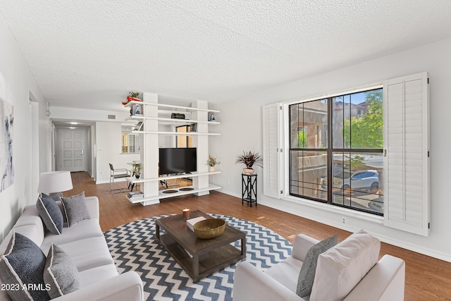 living area with a textured ceiling, wood finished floors, visible vents, and baseboards