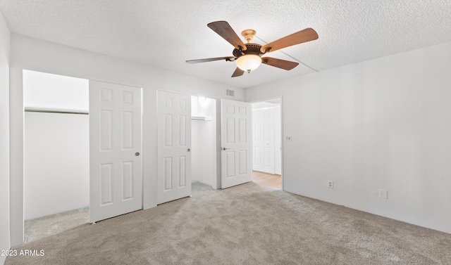 unfurnished bedroom featuring a textured ceiling, visible vents, multiple closets, and carpet flooring