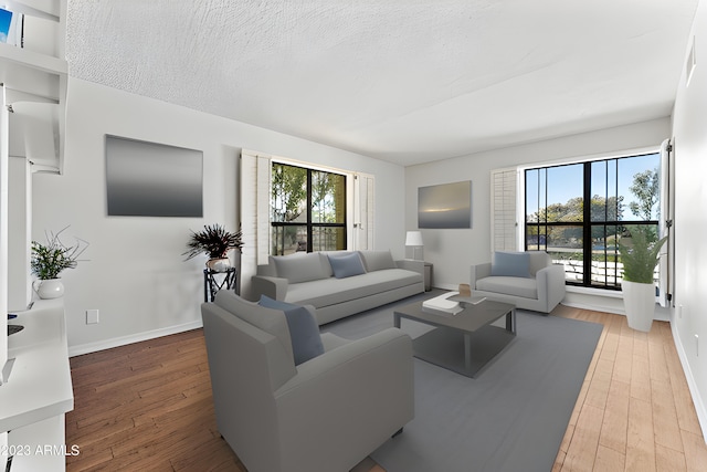 living area featuring light wood-type flooring, a textured ceiling, and baseboards