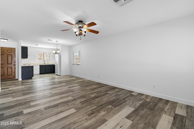 1750 E Desert Rose Trl, San Tan Valley, AZ 85143 - unfurnished living room with visible vents, baseboards, wood finished floors, a sink, and ceiling fan with notable chandelier