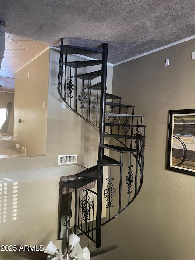 staircase with crown molding, a textured ceiling, and visible vents