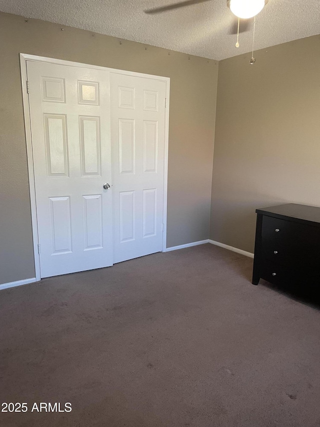 unfurnished bedroom featuring dark carpet, a ceiling fan, a textured ceiling, and baseboards