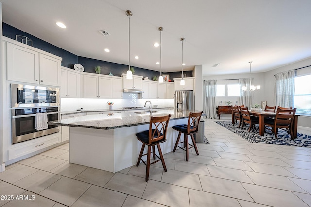 kitchen featuring a spacious island, appliances with stainless steel finishes, white cabinetry, dark stone countertops, and under cabinet range hood