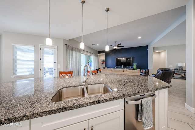 kitchen with stainless steel dishwasher, open floor plan, white cabinetry, a sink, and dark stone countertops