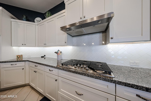 kitchen with tasteful backsplash, dark stone counters, extractor fan, stainless steel gas stovetop, and white cabinetry