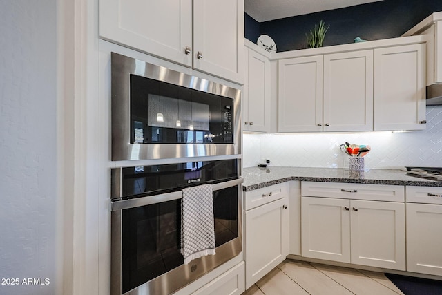 kitchen with light tile patterned floors, tasteful backsplash, white cabinets, stainless steel oven, and built in microwave