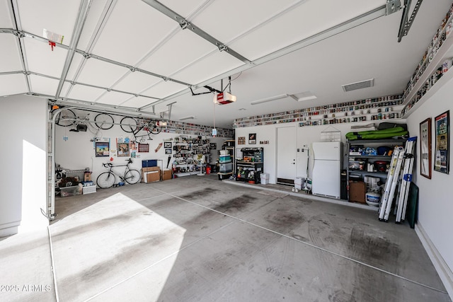 garage featuring visible vents, a workshop area, freestanding refrigerator, and a garage door opener