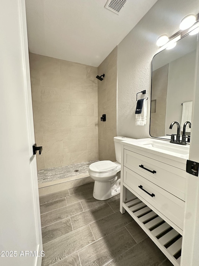 4902 S Fair Ln, Tempe, AZ 85282 - full bathroom with toilet, a tile shower, vanity, wood tiled floors, and a textured wall