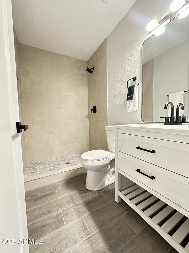 4902 S Fair Ln, Tempe, AZ 85282 - bathroom with toilet, a tile shower, vanity, wood tiled floors, and a textured wall