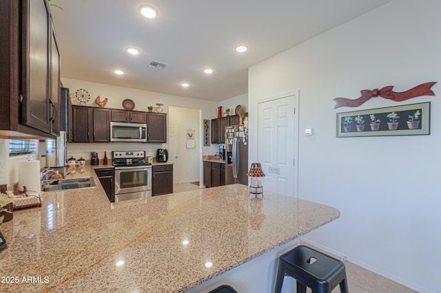 kitchen featuring stainless steel appliances, sink, kitchen peninsula, a breakfast bar area, and light stone countertops