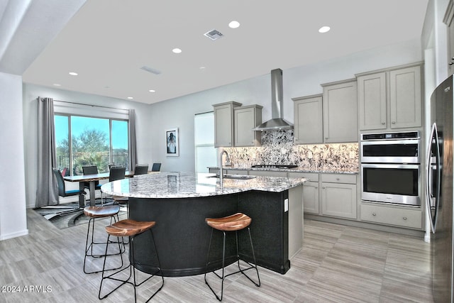 kitchen featuring wall chimney exhaust hood, sink, appliances with stainless steel finishes, and a kitchen island with sink