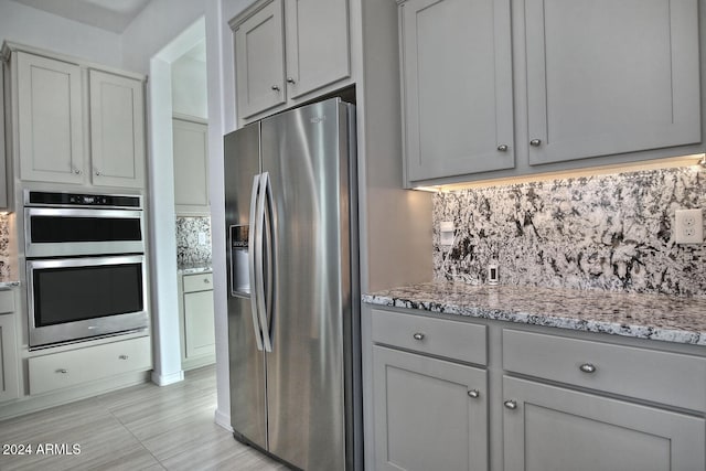 kitchen with gray cabinets, appliances with stainless steel finishes, light stone countertops, and backsplash