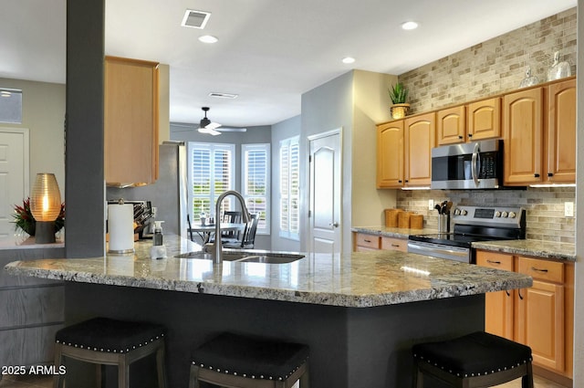 kitchen with stainless steel appliances, a breakfast bar, a peninsula, a sink, and visible vents