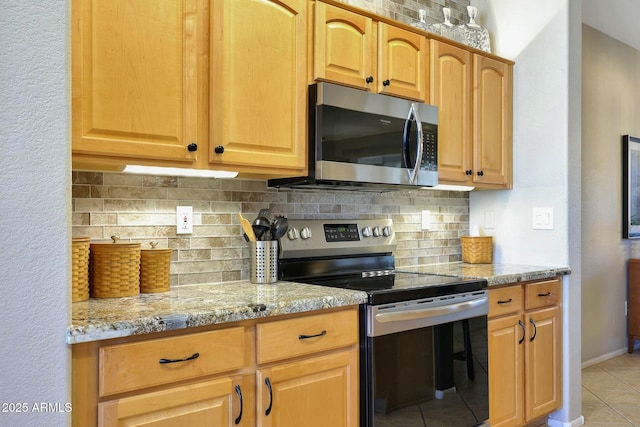 kitchen featuring light tile patterned flooring, stainless steel appliances, baseboards, decorative backsplash, and light stone countertops