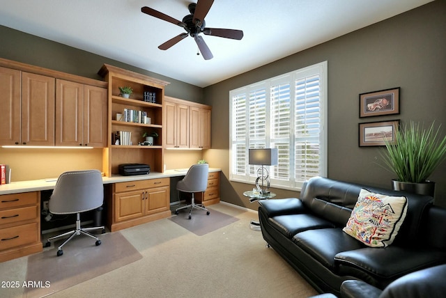 carpeted office space featuring ceiling fan, built in study area, and baseboards