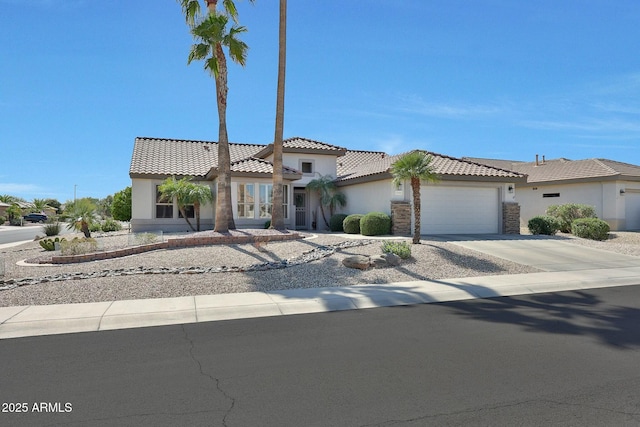 mediterranean / spanish house with a garage, concrete driveway, stone siding, a tiled roof, and stucco siding