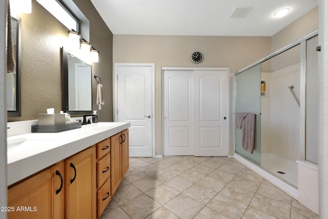 full bath featuring double vanity, visible vents, a sink, a shower stall, and tile patterned floors