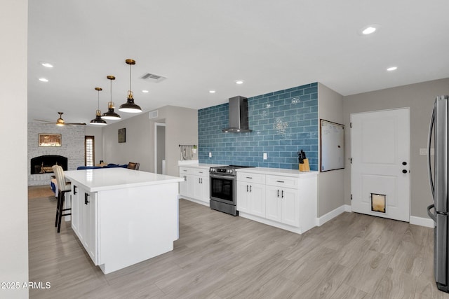 kitchen with appliances with stainless steel finishes, a center island, wall chimney exhaust hood, a fireplace, and decorative light fixtures