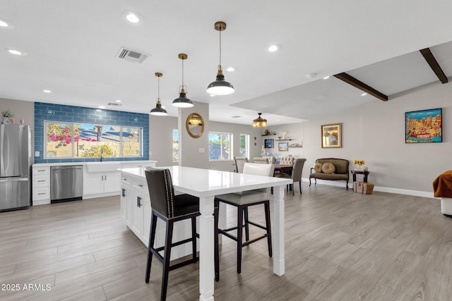 kitchen with appliances with stainless steel finishes, a kitchen bar, a kitchen island, white cabinetry, and decorative light fixtures