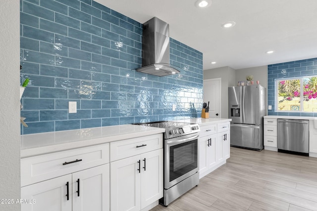 kitchen featuring stainless steel appliances, white cabinets, light hardwood / wood-style flooring, wall chimney range hood, and tasteful backsplash