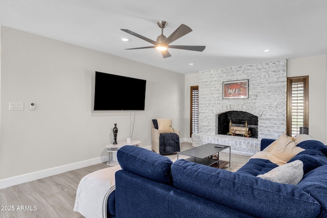 living room featuring ceiling fan, light hardwood / wood-style floors, and a brick fireplace