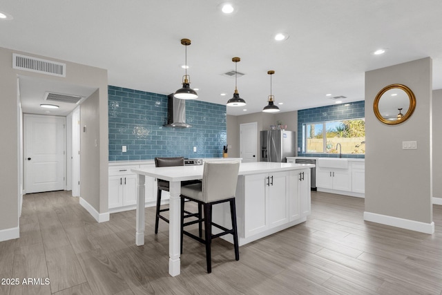 kitchen featuring stainless steel appliances, a center island, wall chimney exhaust hood, white cabinetry, and decorative light fixtures