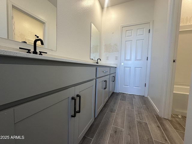 bathroom with wood finished floors, a washtub, double vanity, and a sink