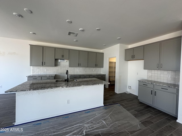 kitchen featuring dark stone counters, tasteful backsplash, a sink, visible vents, and gray cabinets