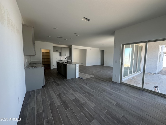 kitchen featuring light stone counters, gray cabinets, dark wood-style flooring, and open floor plan