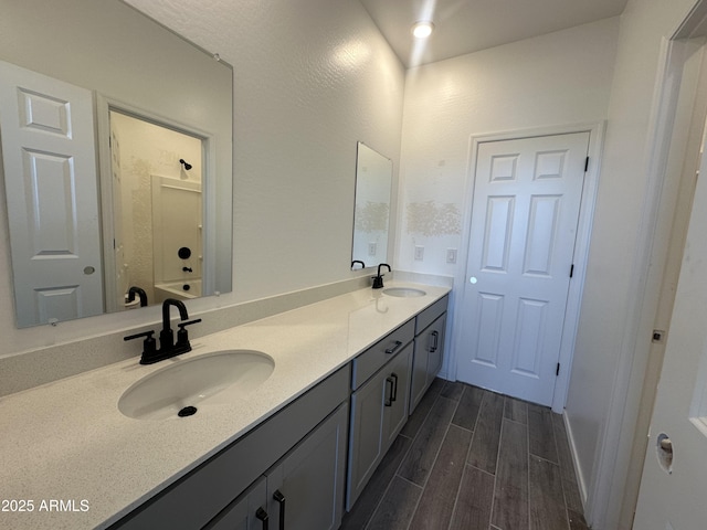 bathroom featuring walk in shower, double vanity, a sink, and wood finished floors