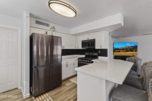 kitchen featuring appliances with stainless steel finishes, light hardwood / wood-style floors, white cabinets, a kitchen bar, and kitchen peninsula