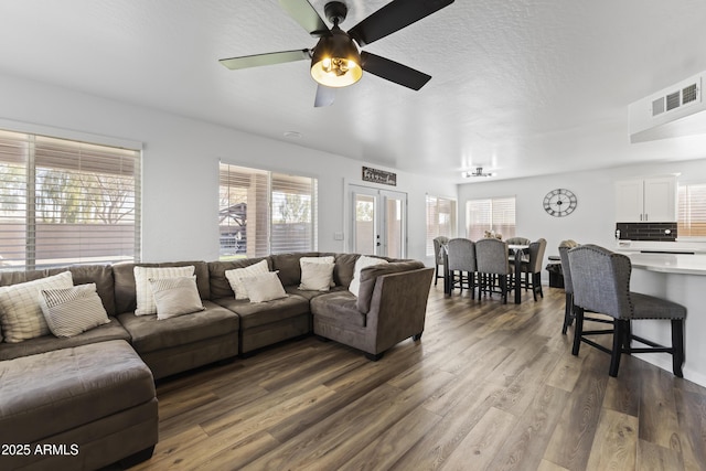 living room with ceiling fan, dark wood-type flooring, french doors, and a textured ceiling