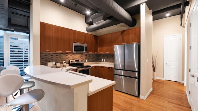 kitchen with kitchen peninsula, appliances with stainless steel finishes, backsplash, a breakfast bar, and light hardwood / wood-style flooring