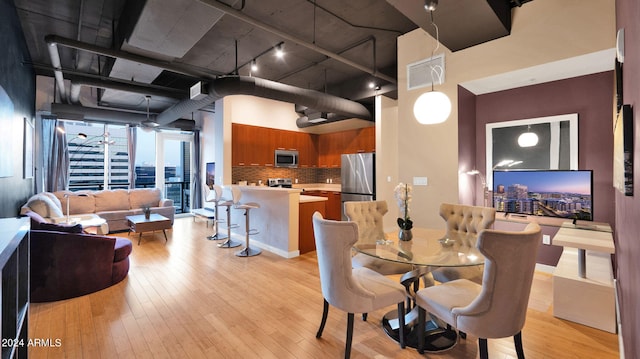 dining space with a towering ceiling, light hardwood / wood-style floors, and track lighting