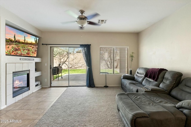 living area featuring visible vents, baseboards, ceiling fan, light carpet, and a fireplace