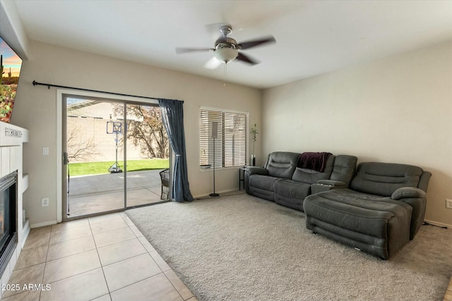 living area featuring baseboards, light colored carpet, light tile patterned floors, a fireplace, and a ceiling fan