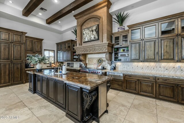 kitchen with tasteful backsplash, dark stone counters, beamed ceiling, range, and a kitchen island