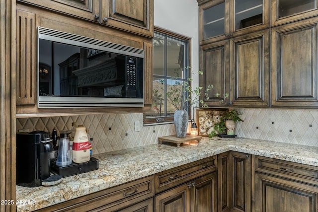 kitchen with light stone counters, stainless steel microwave, and backsplash