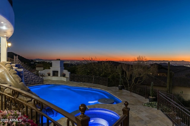 pool at dusk with a patio area, an in ground hot tub, a mountain view, and an outdoor fireplace