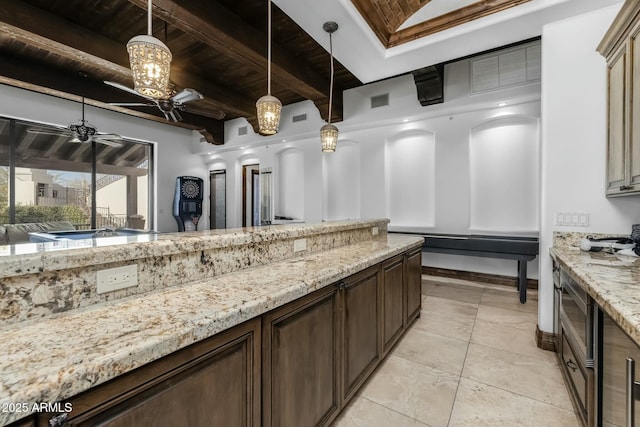 kitchen with beam ceiling, ceiling fan, hanging light fixtures, wooden ceiling, and light stone counters